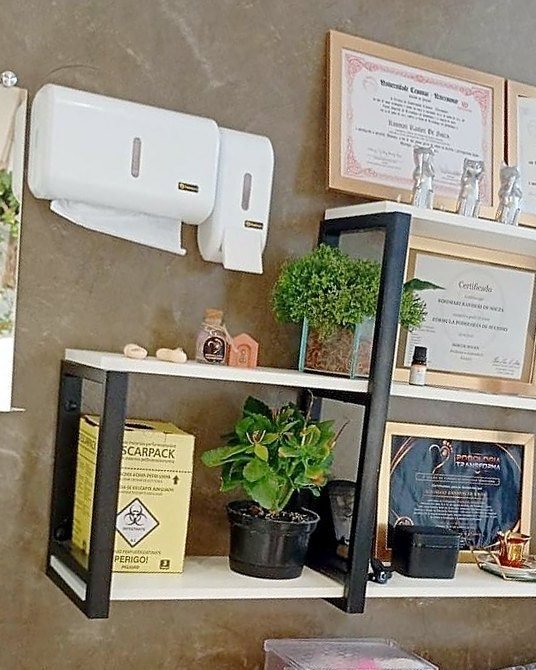 Prateleira do consultório com os certificados da podóloga e a caixa de descarte de material perfurocortante
